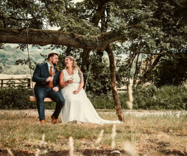 Married couple sit on swing together under large tree